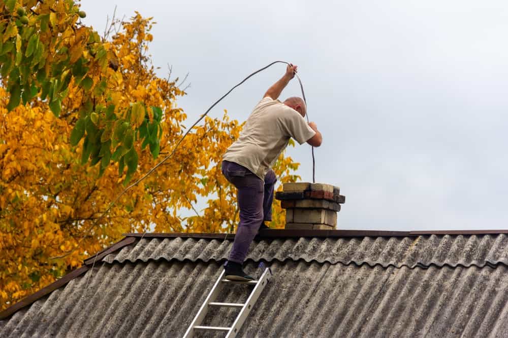 a male chimney sweep cleans the chimney from soot on the roof of a village house, preparation for the heating season
